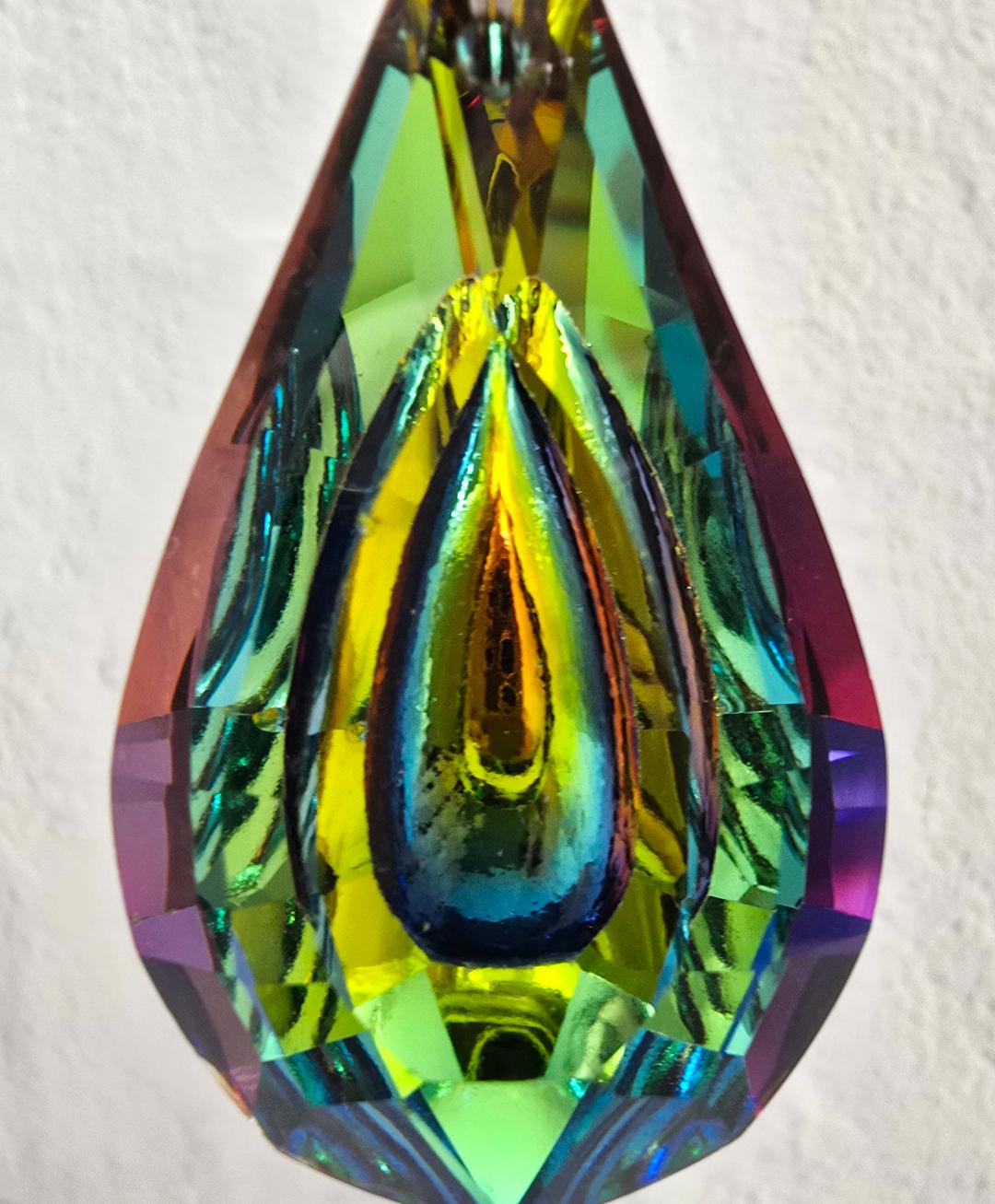 Close-up of the prismatic glass pendant on the Sevenfold Halo suncatcher, reflecting green, blue, and gold light.