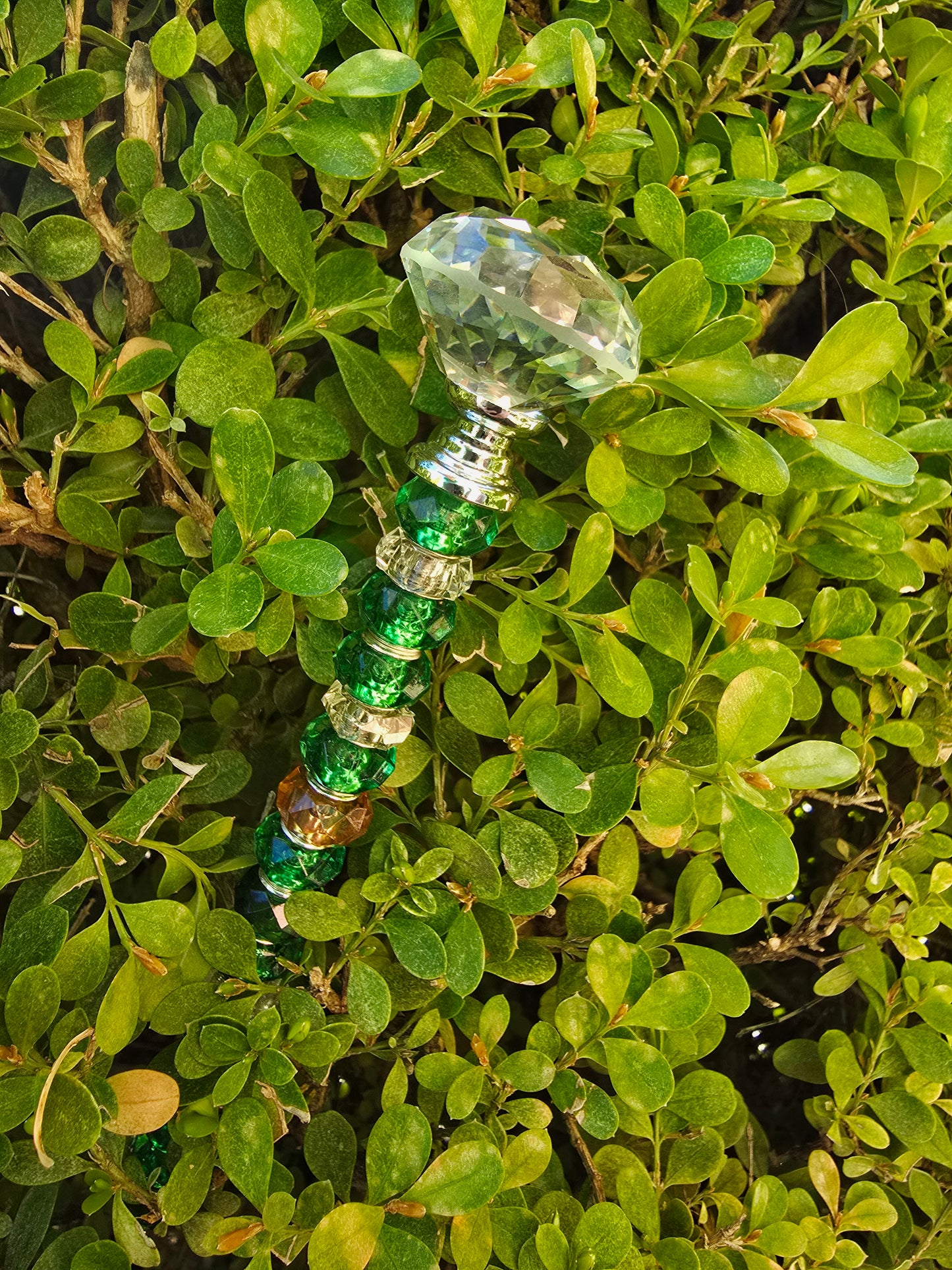 Handmade green glass and acrylic beaded garden stake with crystal-style topper placed among dense spring foliage outdoors.