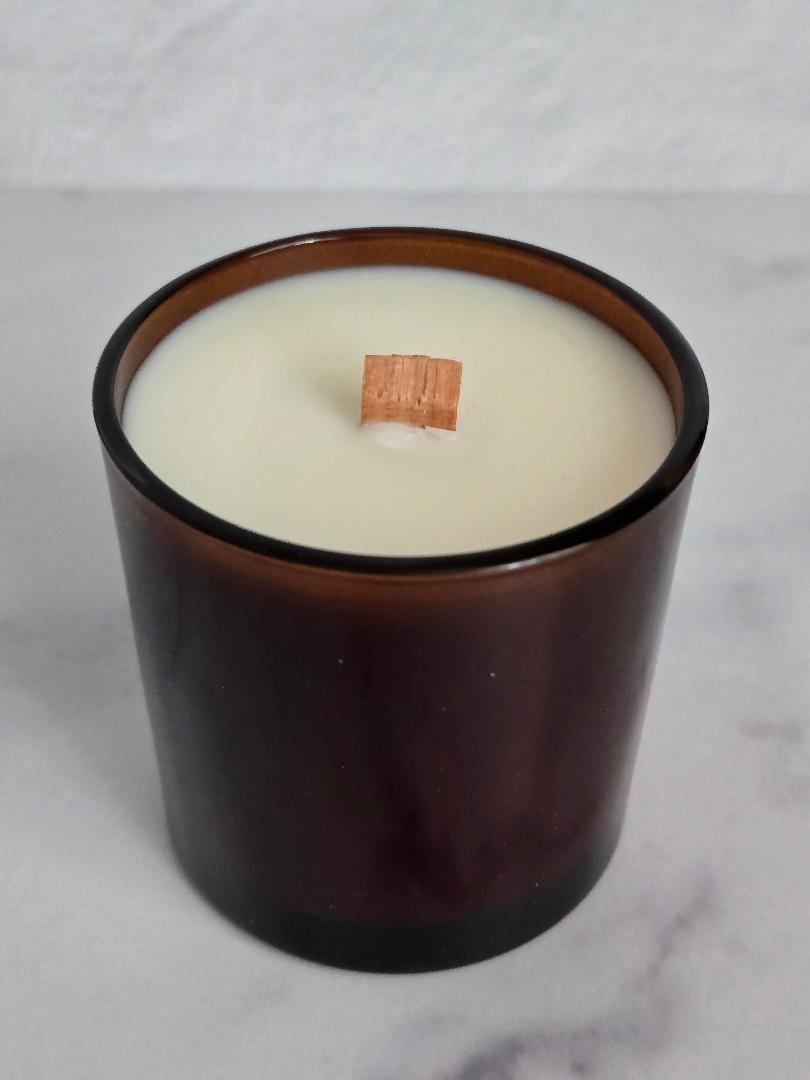 Close-up of coconut soy candle with wooden wick in amber glass jar.