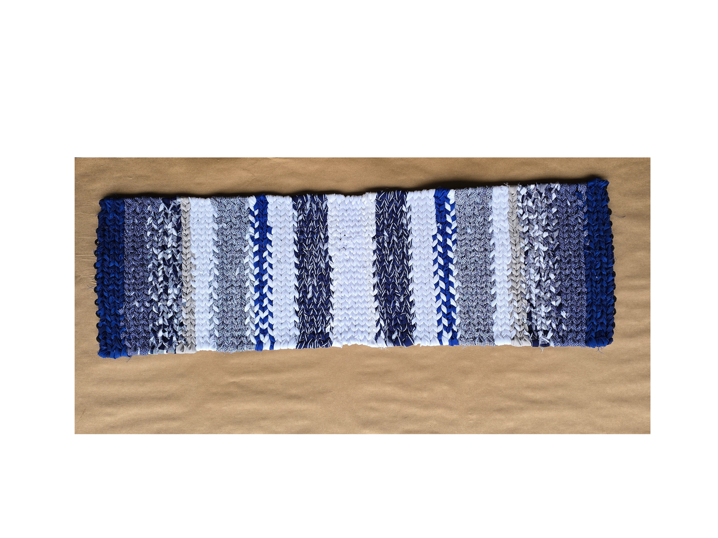 Hand-twined table runner in coastal blues and white displayed on kraft paper background