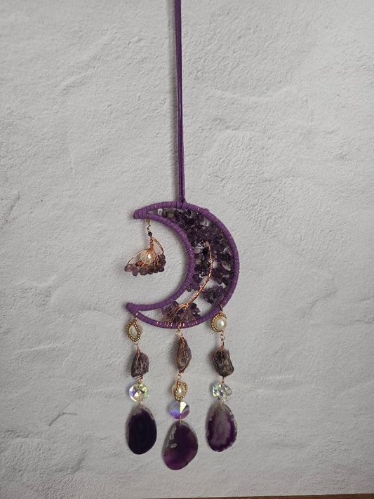 Purple crescent moon suncatcher with amethyst chips, copper wire accents, and three hanging agate slices and crystal prisms, photographed against a light stone background
