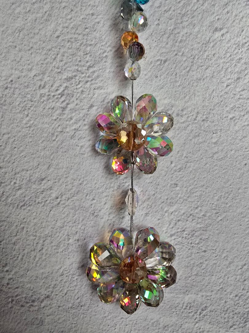 Close-up of the Twin Petal Cascade suncatcher showing both layered iridescent crystal flowers and the shimmering multicolor accent beads