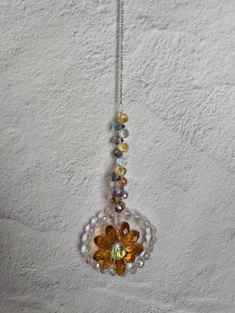 Floral Radiance Suncatcher with a warm amber-gold faceted crystal flower surrounded by clear crystals and a golden-tone iridescent beaded stem
