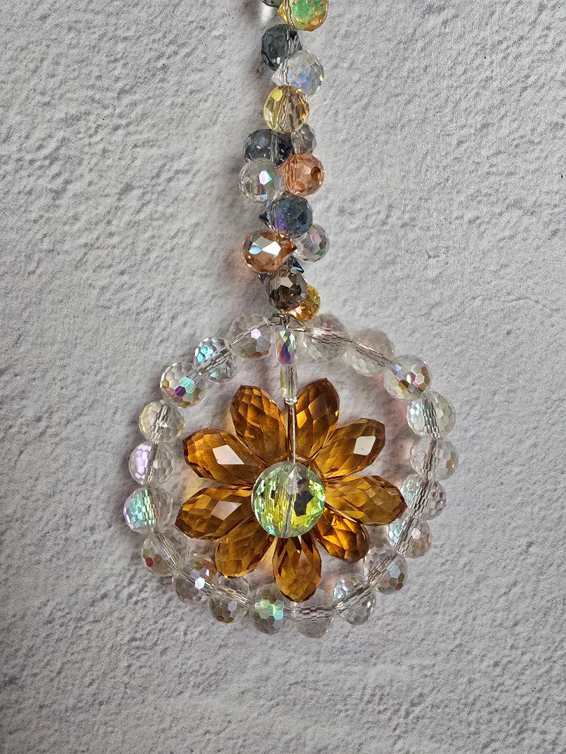 Close-up of the Honeyglow Aura Bloom suncatcher showing the amber crystal petals, center stone, and reflective accent beads