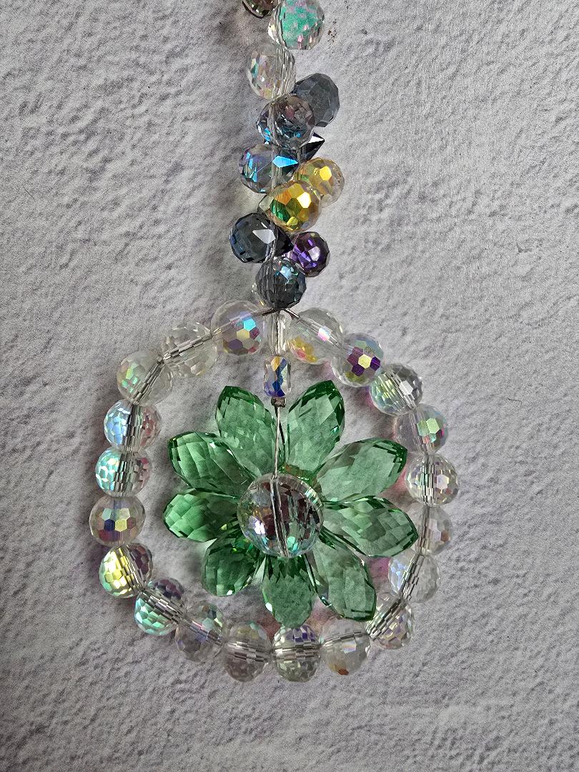 Close-up of the Verdant Light Bloom suncatcher highlighting the green crystal petals, central round crystal, and shimmering beadwork