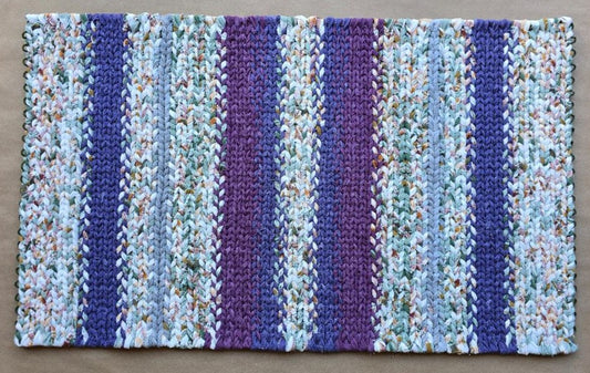 Hand-twined rectangular rug in cool tones of blue, lilac, and deep amethyst, featuring alternating vertical bands of flannel and brushed-cotton textures. The rug measures approximately 40 by 24 inches and has a soft, misty, blended appearance.
