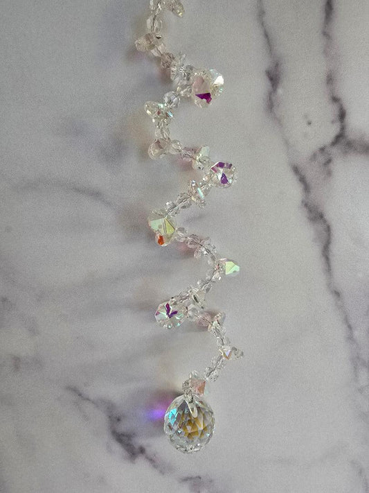 Aurora Spiral crystal suncatcher with a twisted helix design, hanging against a marble background, showing clear AB-coated crystals that reflect soft rainbow light