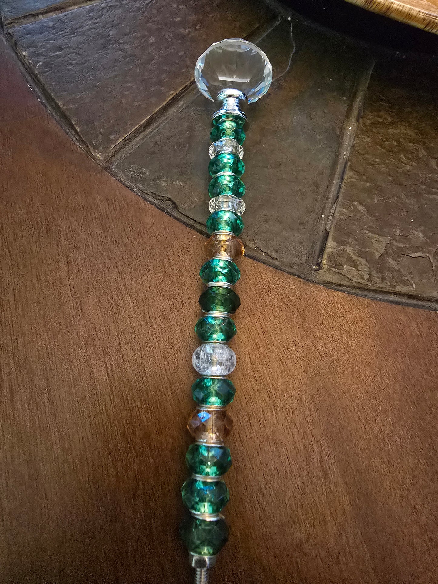 Completed green beaded garden stake with faceted crystal-style topper displayed on a wooden tabletop.