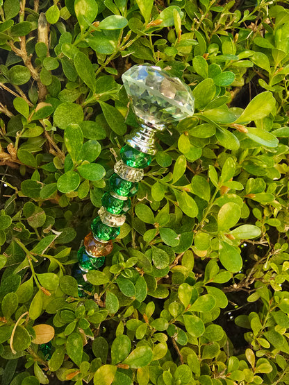 Handmade green glass and acrylic beaded garden stake with crystal-style topper placed among dense spring foliage outdoors.