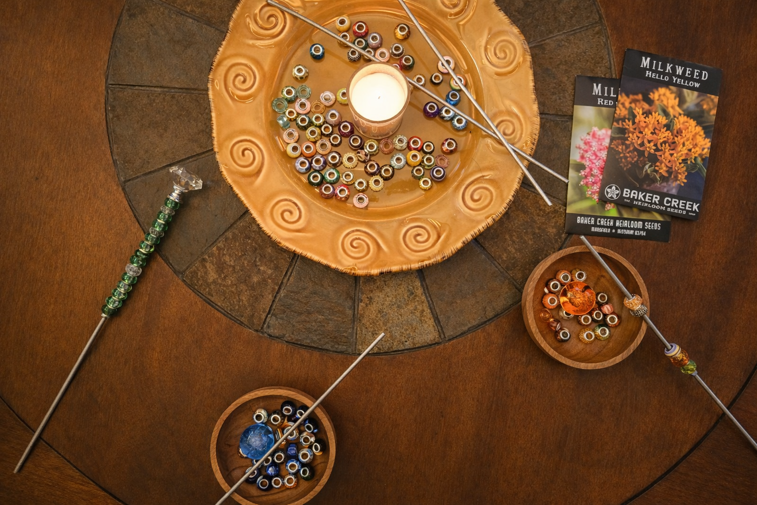 Spring equinox garden gathering kit with beads, metal rods, lit candle, seed packets, and partially assembled garden stakes arranged on a wooden table.