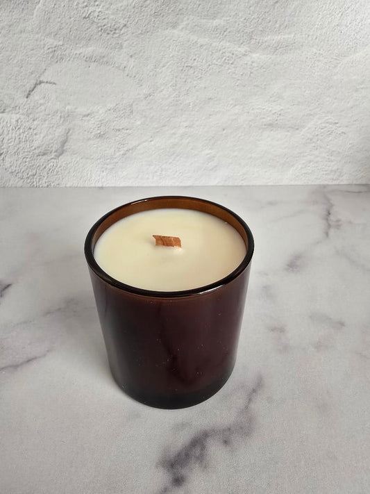Amber glass coconut soy candle with wood wick on white marble background.
