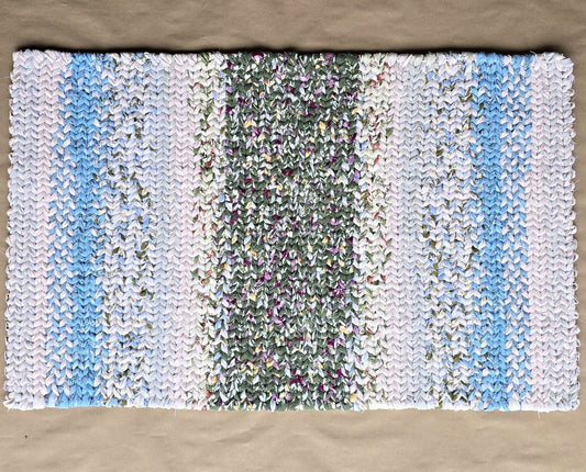 A hand-twined rectangular flannel rug with a mossy green textured center and soft gradients of white and sky blue on both sides, displayed on kraft paper.