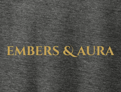 Close-up of the Embers & Aura gold logo printed on the front of a gray tri-blend T-shirt.