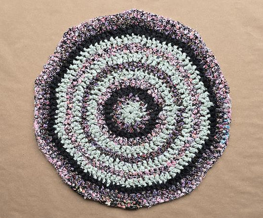 Hand-knotted circular rug named Secret Garden, made using the traditional Amish Knot technique. Features concentric rings in black, pale green/white, and dark pink. The rug is approximately 28 inches in diameter.