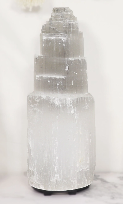 Tall tiered selenite tower lamp on a marble surface, unlit, showing natural white striations.