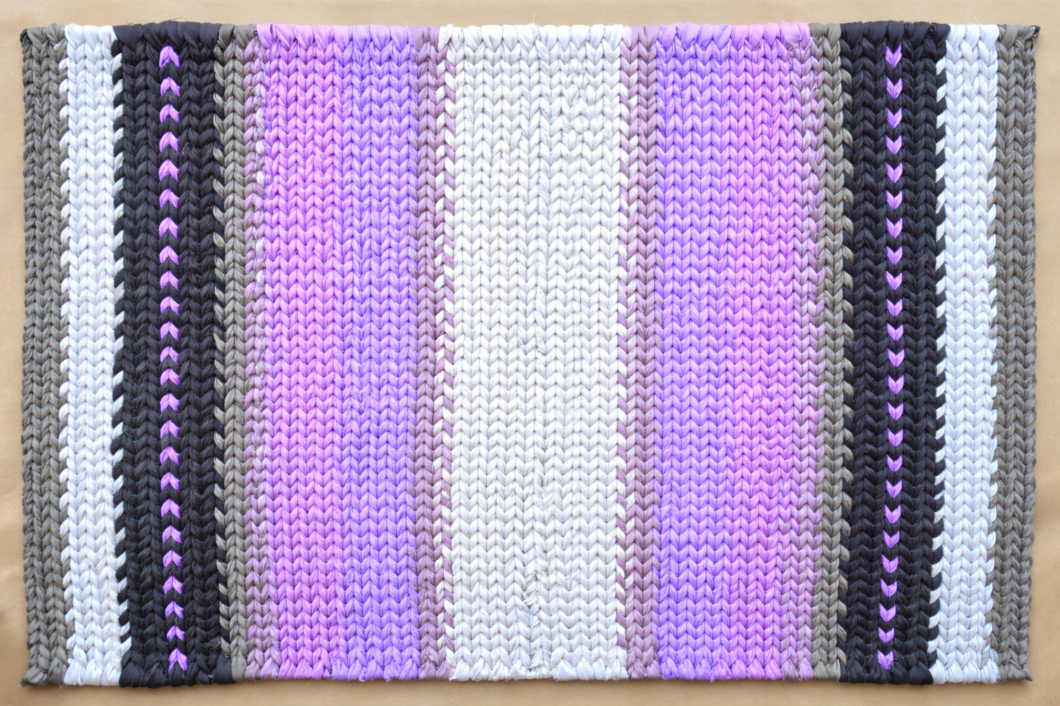 Hand-twined rectangular rug in black, gray, and layered violet tones, with subtle heart-shaped accents woven into the design.