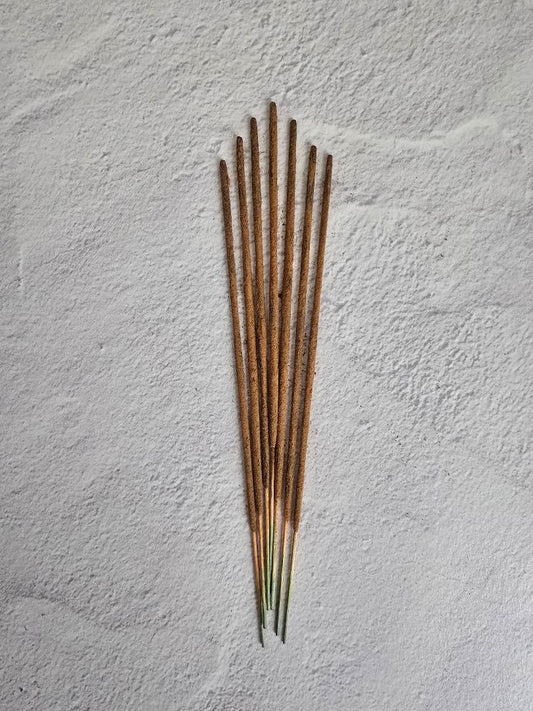 Seven natural incense sticks arranged in a fan shape on a textured white background