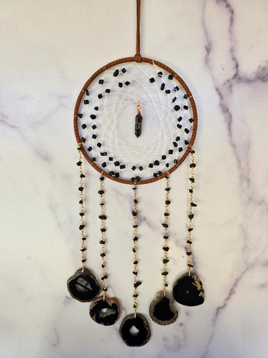 Handcrafted obsidian and agate wall hanging with a woven center, wrapped crystal point, and five cascading stone strands displayed against a neutral background.