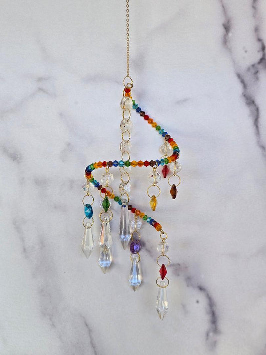 Hanging spiral suncatcher with rainbow glass beads and crystal drops on a soft marble background