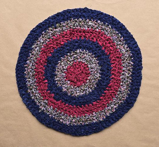 Hand-knotted circular rug named Midnight Bloom, made using the traditional Amish Knot technique. Features concentric rings in deep navy blue, rich burgundy, and multi-colored fabric. The rug is approximately 28 inches in diameter.